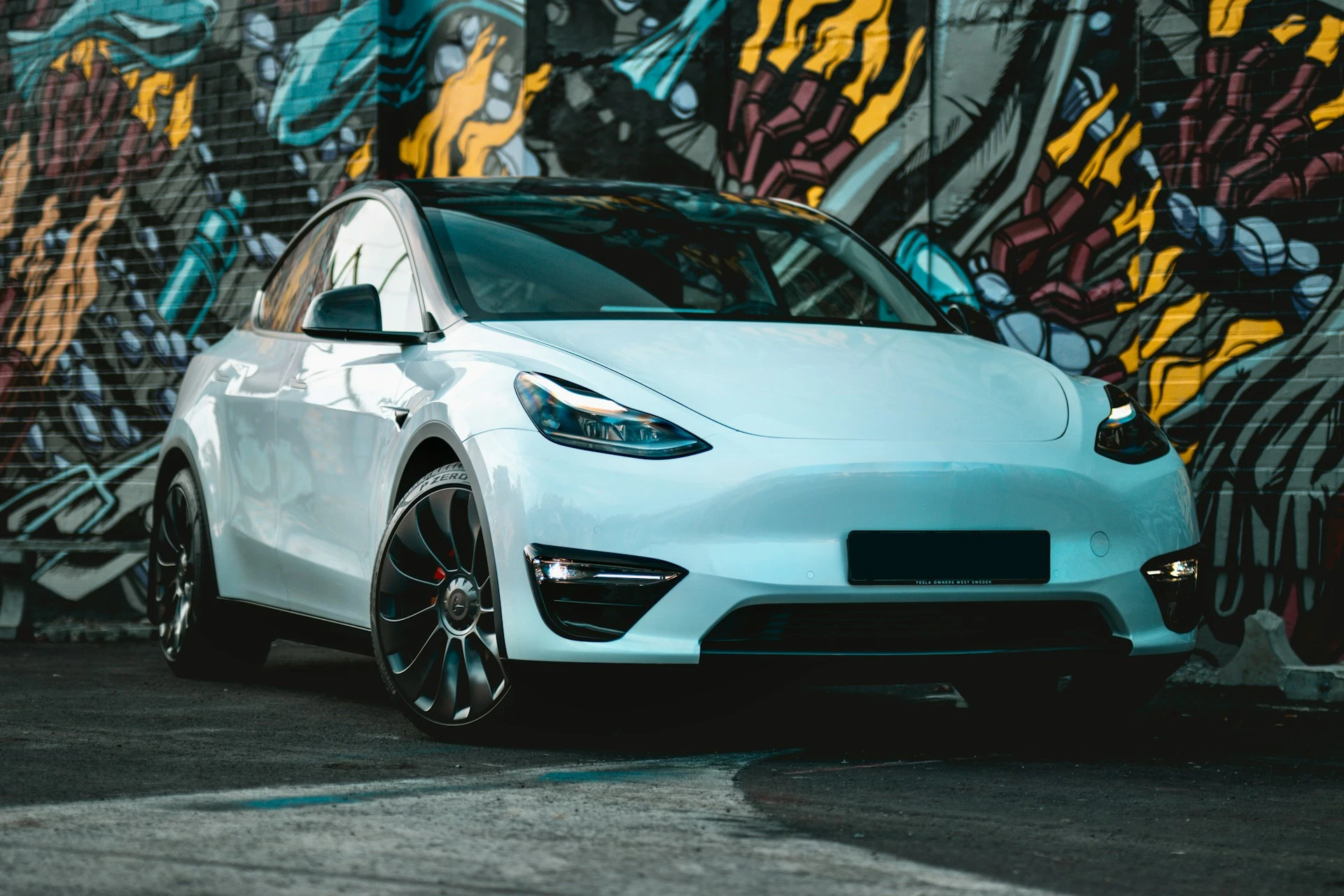 Tesla Model Y alb parcat în fața unui perete colorat cu graffiti, unul dintre cele mai populare modele de mașini electrice în România